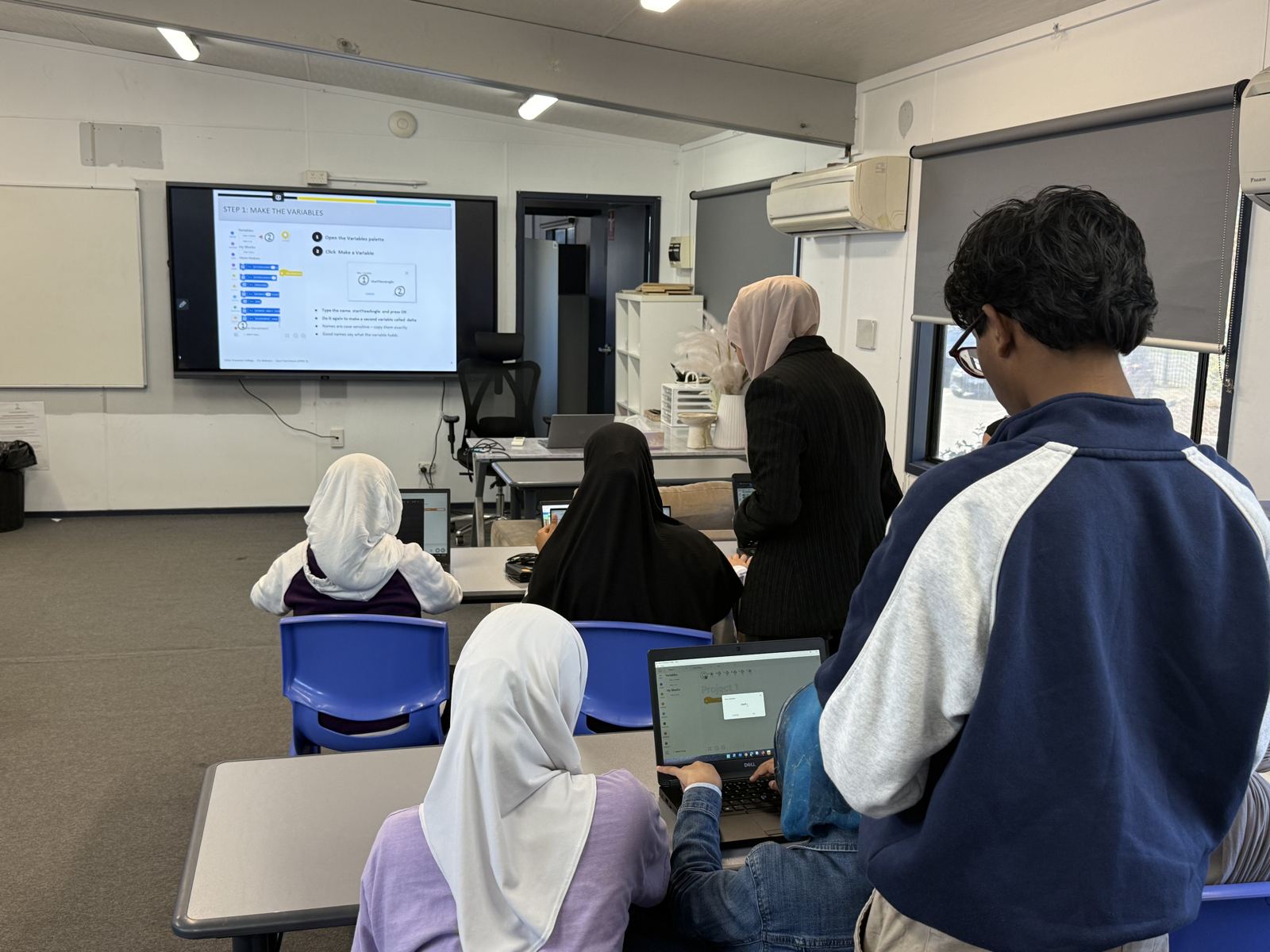 Students coding on laptops while a mentor helps